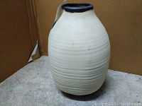 Front view of off-white ceramic pot with horizontal ridges and black rim.