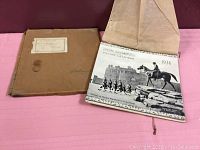 Photo showing the calendar partially open with original brown shipping package beside it on a pink surface