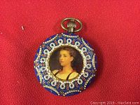 Front closed view of pocket watch showing blue enamel casing with decorative white and red bead jewels and central portrait of a woman.
