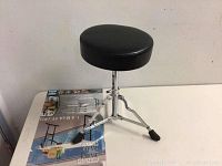 Side angle showing full stool with black round padded seat and adjustable tripod chrome legs with rubber feet.