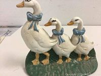 Side angle view of the cast iron doorstop showing three white geese with blue bow ties standing on a green base.