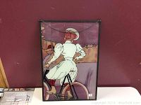 Frontal view of the stained glass panel featuring a girl on a bicycle, showing the full piece with metal frame and hanging chain, set against a maroon background.