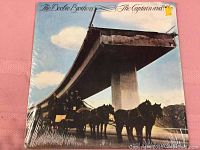 Front cover of The Doobie Brothers The Captain And Me album in shrink wrap shows horse-drawn carriage under an unfinished highway.