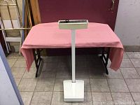 Full view of the white Detecto Doctor's Scale standing on tiled floor with a pink cloth-covered table behind it