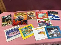 Top view of all 10 children's books arranged on a pink cloth surface showing colorful illustrated covers and French titles.