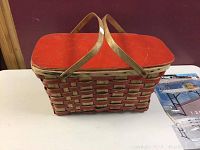 Front and side view of vintage picnic basket showing woven body, red wooden lid, and wooden handles.
