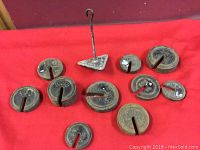 Full view of all 10 cast iron scale weights arranged on a red cloth with a metal hanger in the center.