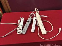 Four power bars on red surface, showing two Nomad white bars and two Belkin bars (gray and white).