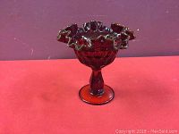Side view of the ruby red glass candy dish showing ruffled edge and pedestal base on red background.