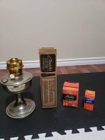 Full view of vintage Aladdin metal oil lamp with brass burner, boxed chimney, and unopened parts boxes