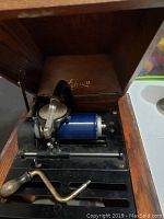 Wooden cabinet open to show Edison phonograph mechanism with a blue cylinder record in place