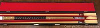 Full view of assembled pool cue in its case showing wood and black wrap grip.