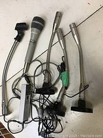 Top view of the full lot of five vintage microphones with wires and metal bases on a white surface.