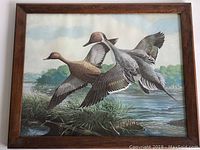 Full view of the vintage framed print depicting two flying ducks above a marsh scene, framed in wood.