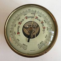 Front view of brass barometer with dial reading showing pressure scale and weather conditions