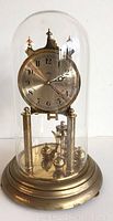 Full view of the anniversary clock with glass dome, brass base, and rotating pendulum.