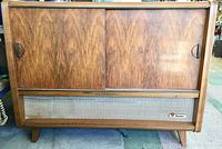 Front view of vintage wooden stereo cabinet with sliding doors closed, showcasing mid-century wood finish and speaker cloth grille.