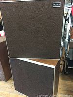 Two vintage Sony speakers stacked, showing front grille and wood panel sides.