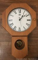 Full view of the wooden wall clock mounted on a wall, showing the octagonal frame and pendulum section below.