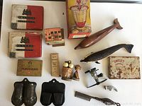Vintage miscellaneous lot items including tins, wooden decorative pieces, toys, comb, metal shoe molds, and small mechanical devices arranged on a flat surface.