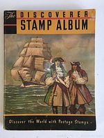 Front cover of The Discoverer Stamp Album showing illustration of two men in 17th-century attire with a sailing ship in background, album title and tagline visible.