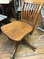 Full view of vintage solid oak office chair showing wooden seat, slatted backrest, and four-legged swivel base with castors.