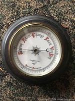 Close-up of antique barometer face showing detailed dial and maker's name