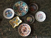 Overview of the seven plates and dishes showing varied decorative motifs including flowers, lemons, and scenic themes in different sizes and shapes.