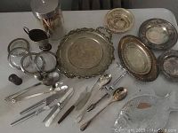 Full lot of assorted silverplate trays, plates, cutlery and serving utensils displayed on white surface
