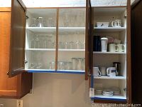 Cupboard with upper shelves stocked with stemware, drinking glasses, and coffee mugs including Dansk