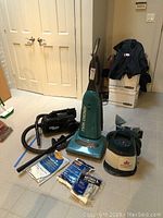 Photo showcasing the Sharp Twin Energy upright vacuum, Eureka The Boss Mightymite canister vacuum, Bissell Little Green steamer, and vacuum bags on floor.