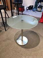 Side angled view of round frosted glass top designer side table by Zack with stainless steel base on carpeted floor, showing table height and structure.