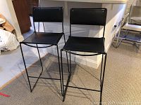 Two black metal bar stools placed side by side in front of a counter. Photo shows overall condition and design.
