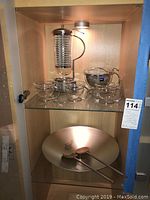 Cabinet overview showing top shelf coffee and tea set and bottom shelf salad bowl with utensils