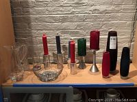 Alessi wire basket bread bowl, four candleholders with different colored candles, and additional metal and glass candleholders displayed on wood shelf