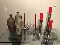 Wide shot of all items in the lot including tall painted vases, stainless steel candleholders with red candles, and clear Nambe glass vase on a glass table