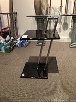 Side table angled showing black lacquer top and chrome vertical supports.