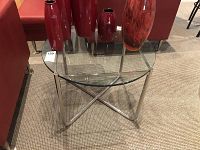 Side table shown with glass top and chrome frame with red decorative items on top.