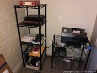 Photo of shelving unit with multiple electronic devices and office supplies including the HP printer and other items.