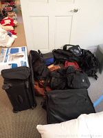 Photo showing multiple black and leather bags including two Tumi roller luggage pieces and other duffels and backpacks.