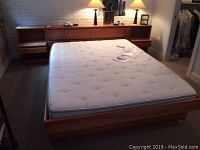 Full view of queen bed with mattress and headboard against white brick wall