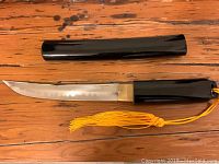 Full ceremonial blade with sheath and yellow tassel on wooden surface