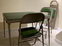 Photo showing the folding table with green vinyl top and three of the four matching folding chairs with green vinyl padded seats and backs arranged around it.