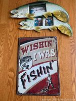Two fish-shaped picture frames with three photos each above a vintage style metal sign with fishing text.