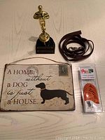 All items displayed together on a white surface showing the leash, booties, metal dog sign and trophy