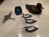 Full lot view showing wooden duck decoy with three metal loons and one metal ray figurine on a table surface.