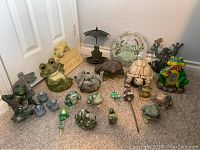 Full assortment of frog-themed garden decor showing various statues, bird feeder, wind chimes, and plaque on floor by door.
