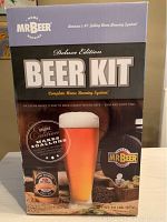 Photo of the front of the Mr. Beer Deluxe Edition Beer Kit box showing product branding, beer image, and brewing system features.