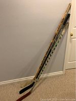Three hockey sticks leaning against wall showing full length and blade condition