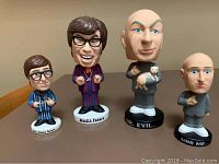 Photo showing all four bobbleheads on a table with two Austin Powers figures, Dr. Evil holding a white cat, and Mini Me, all standing on labeled bases.